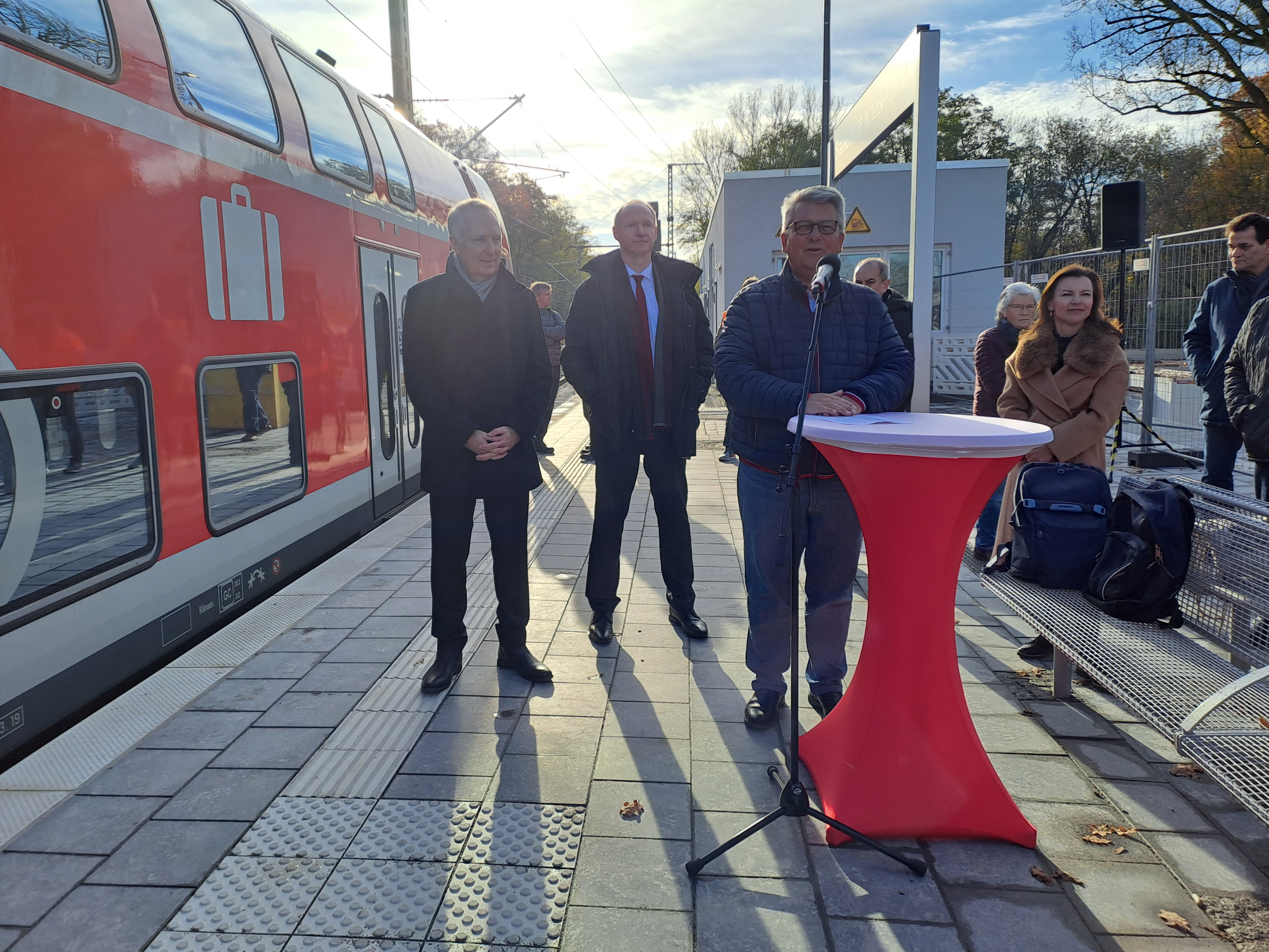 Inbetriebnahme am Gleis, Redner am roten Stehtisch, Menschen im Hintegrung