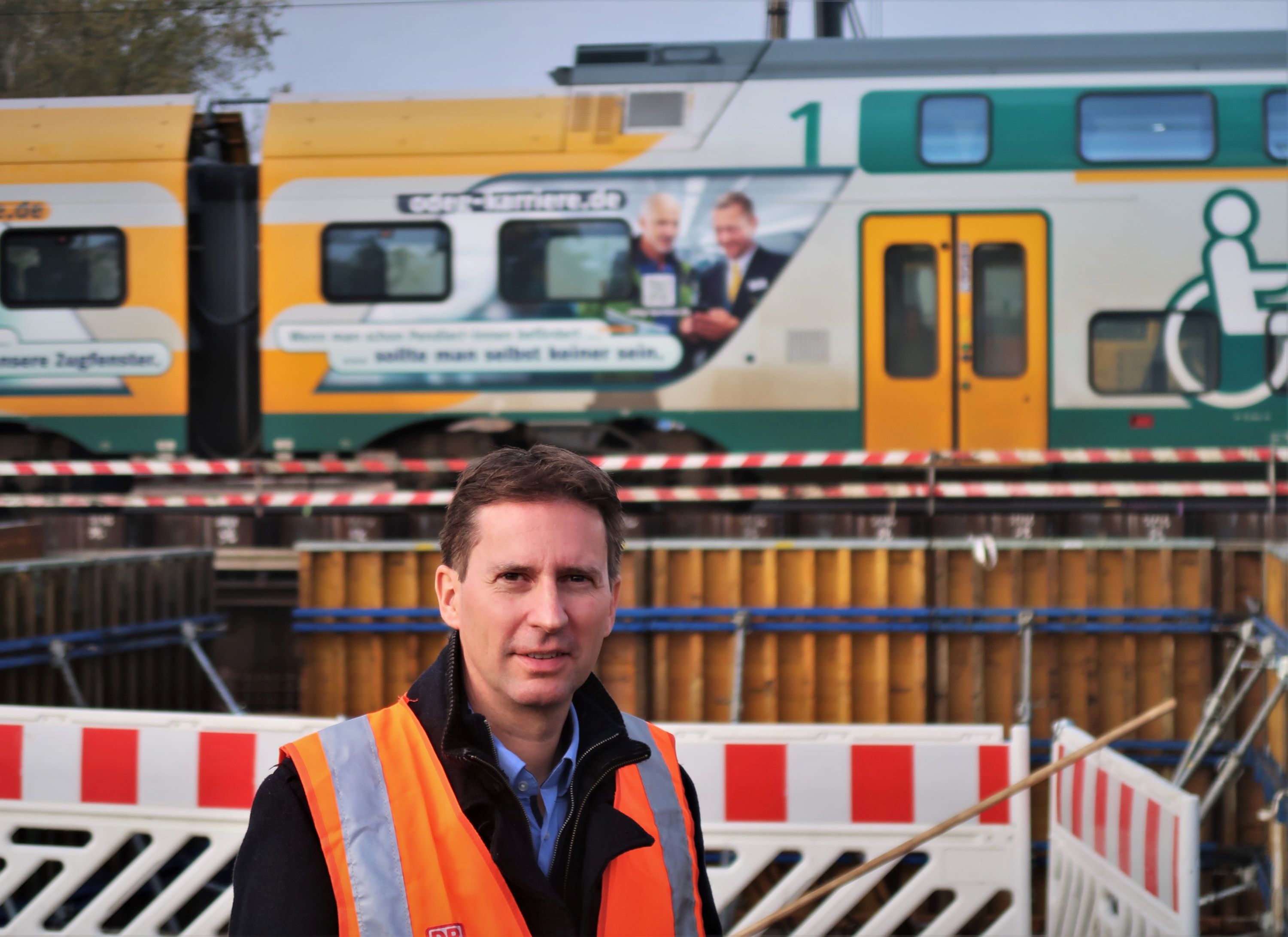 Bild zeigt Martin Ludwig in Warnweste vor abgegrenzter Baustelle und Zug